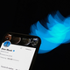 A phone with Elon Musk's Twitter profile is shown against a black background along with a blurred Twitter logo.
